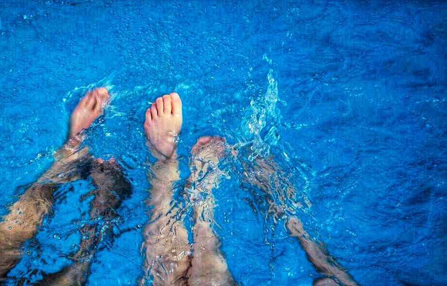 Planschende Beinpaare in leuchtend blauem Wasser.