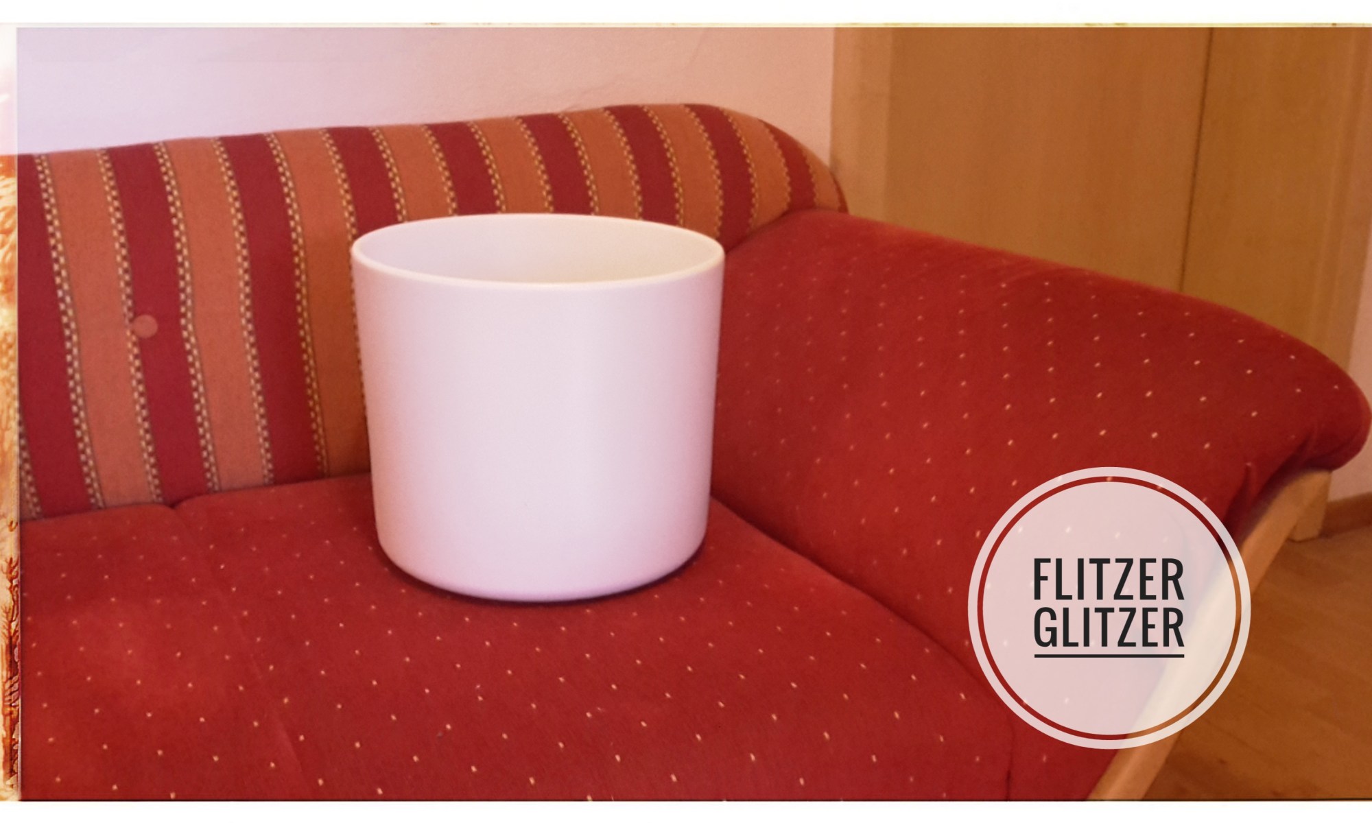 Einfacher weißer Übertopf auf rotem Sofa.