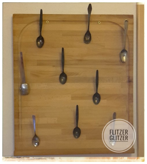 Holzbrett, auf dem Löffel angeschraubt wurden. Mit den Griffen nach oben, damit sich daran Jacken aufhängen lassen.